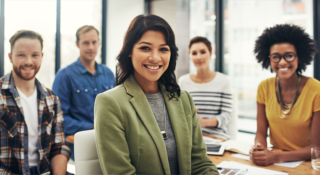 People sitting at a conference table all turned to face the camera and smile