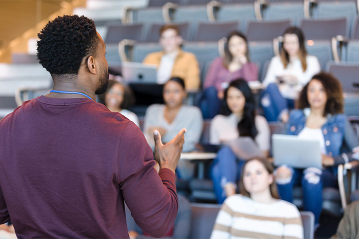 Behind a man speaking to a class.